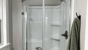 Eine gläserne Dusche mit Duschbrause, Handtuchhalter und Fenster.
