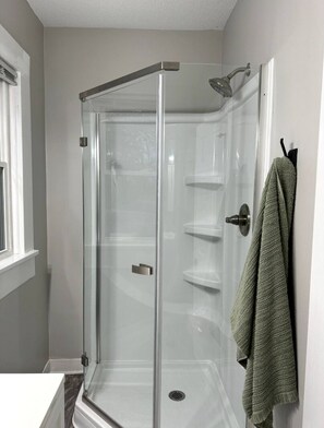 Eine gläserne Dusche mit Duschbrause, Handtuchhalter und Fenster.