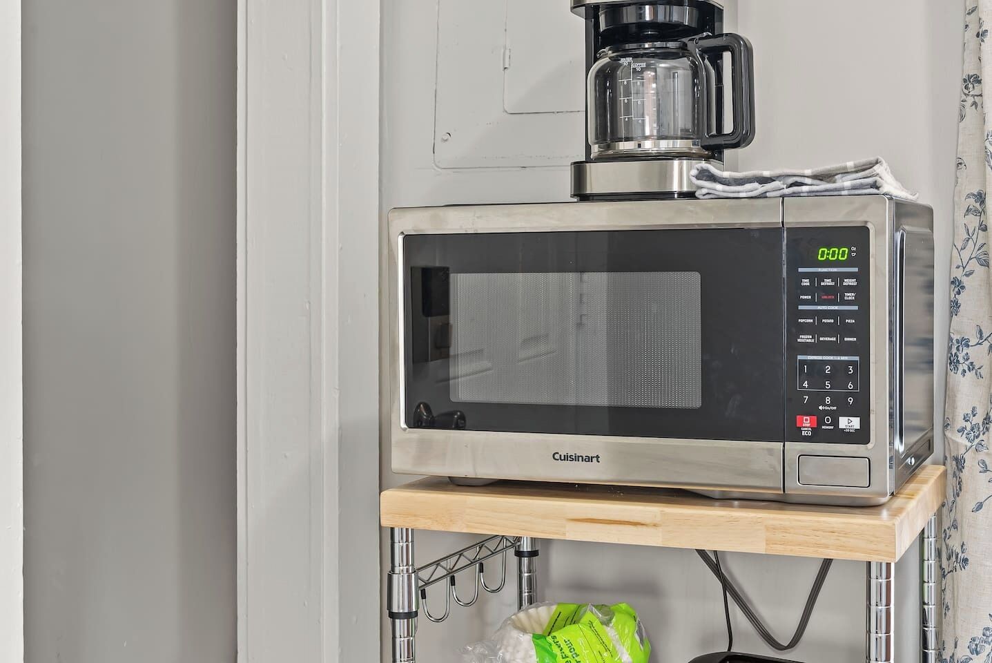 A microwave oven with a digital display and control panel, placed on a wooden shelf.