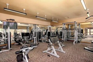 Ein Fitnessstudio mit verschiedenen Trainingsgeräten, Spiegeln und einem Fernseher.