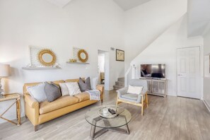 Ein Wohnzimmer mit Sofa, Sessel, Glastisch und Fernseher.