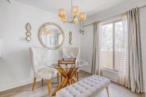 A room with a round glass table, two chairs, a bench, a chandelier, a large mirror, and a window with curtains. - Golf Course Condo, Mountain Views, Old Town (Scottsdale)