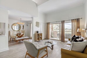 A spacious living room with a dining area, a sofa, a coffee table, and a view through large sliding doors. - Golf Course Condo, Mountain Views, Old Town (Scottsdale)