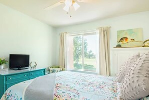 Ein Schlafzimmer mit Bett, Fernseher, Schreibtisch und einem Fenster mit Vorhängen.