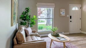 A living room with a leather sofa, a coffee table, and a large window with a view of a tree and a house.