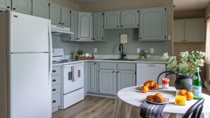 A kitchen with light green cabinets, a white refrigerator, a stove, and a dining table set with food and drinks.