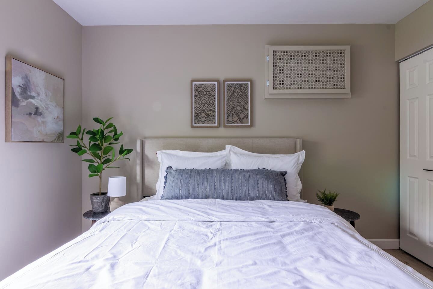 A bedroom with a bed, a nightstand, a potted plant, and a wall-mounted air conditioning unit.