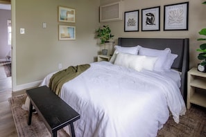 A bedroom with a bed, bedside tables, a bench, and wall art.