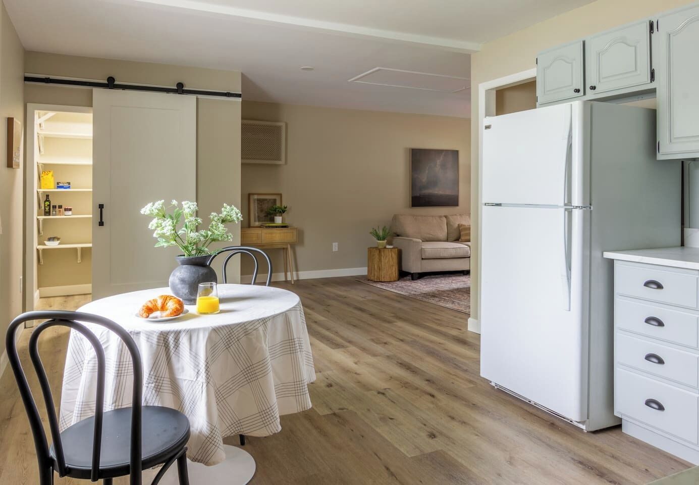 A compact kitchen with a dining area, a refrigerator, and a sofa in the background.