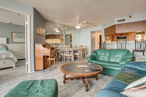 A living room with a green sofa, a wooden coffee table, and a dining area with chairs and a piano. - Beachfront Condo! Heated Pool, Ocean-View Balcony (Daytona Beach Shores)