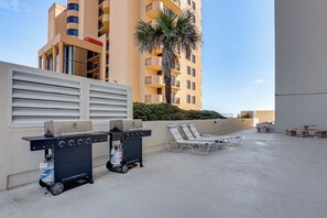 Eine Terrasse im Freien mit zwei Grillanlagen, Liegestühlen und einer Palme.