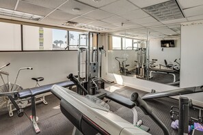 Ein Fitnessstudio mit Trainingsgeräten, einem großen Spiegel und einem Fenster mit Blick auf Palmen.