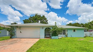 A single-story house with a garage, a front yard with grass and a paved driveway, and a clear sky with clouds. - Lanai, Pool Access! Naples Studio Near Beach (Naples)