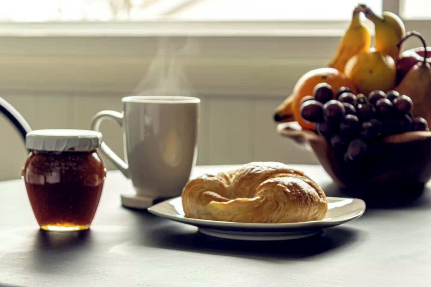 Una mesa con un croissant, una taza y un bol de fruta.
