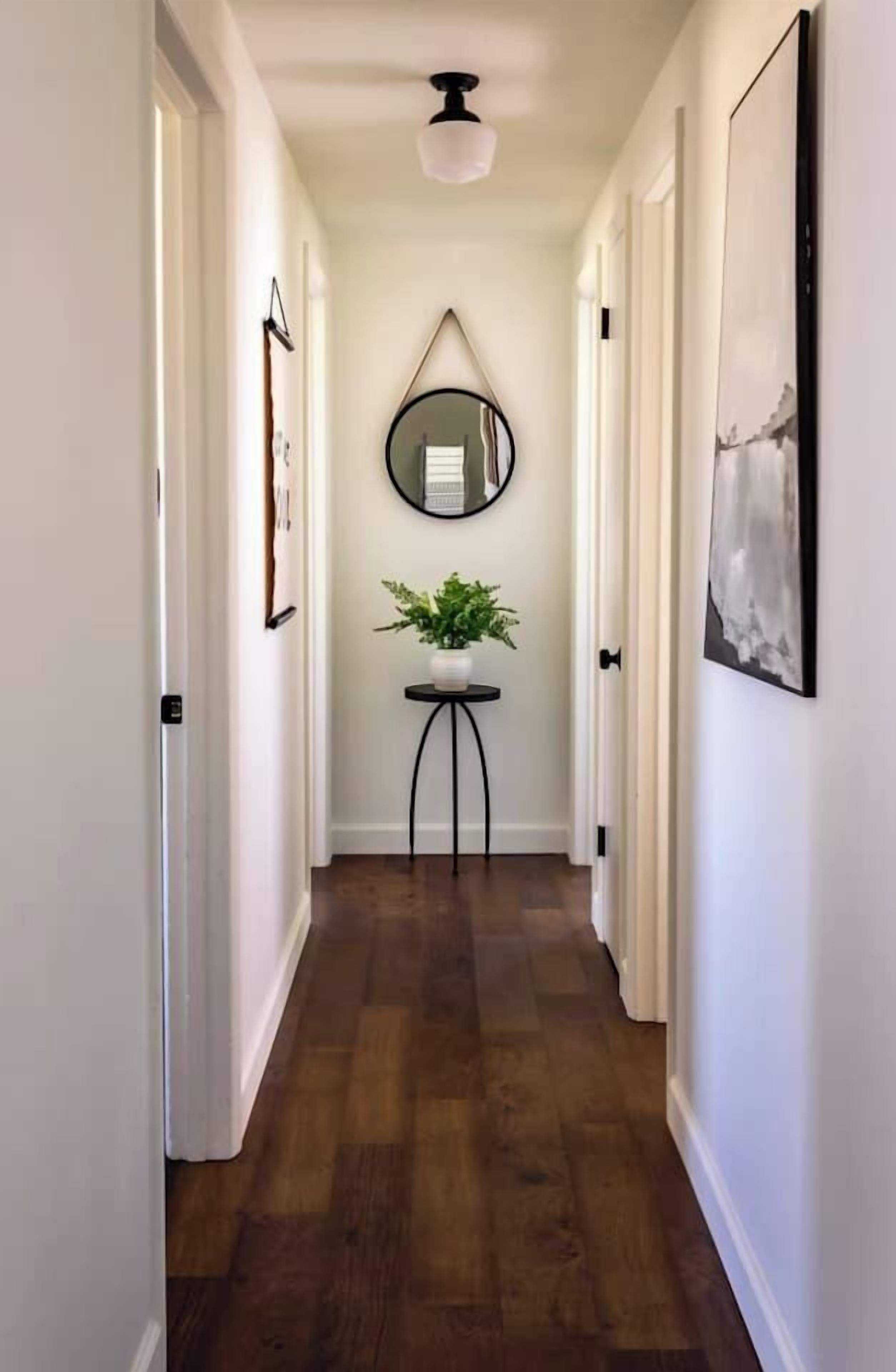 A hallway with a round mirror on the wall, a small table with a plant, and a framed picture on the right.
