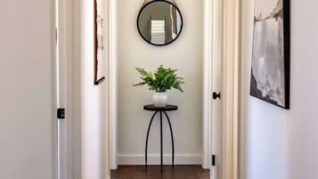 A hallway with a round mirror on the wall, a small table with a plant, and a framed picture on the right.