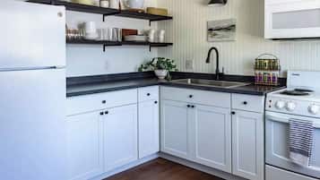 A kitchen with white cabinets, a black countertop, a sink, a stove, and shelves with kitchenware.