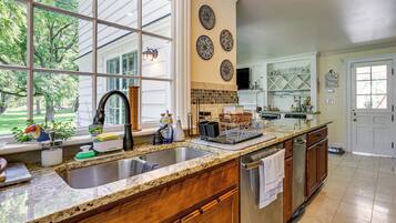 A kitchen with a large window, a stainless steel sink, wooden cabinets, and a tiled backsplash.