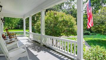A covered porch with a white railing, a rocking chair, and an American flag.