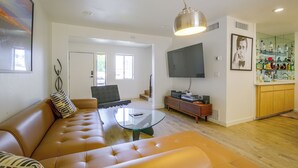 A modern living room with a leather sofa, a glass coffee table, a flat-screen TV, and a kitchen area with wooden cabinets and a wine rack. - Walk to El Paseo Shops! Palm Desert Condo w/ Patio (Palm Desert)
