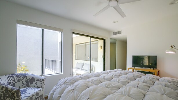 A bedroom with a large bed, a chair, a television, and a ceiling fan. - Walk to El Paseo Shops! Palm Desert Condo w/ Patio (Palm Desert)