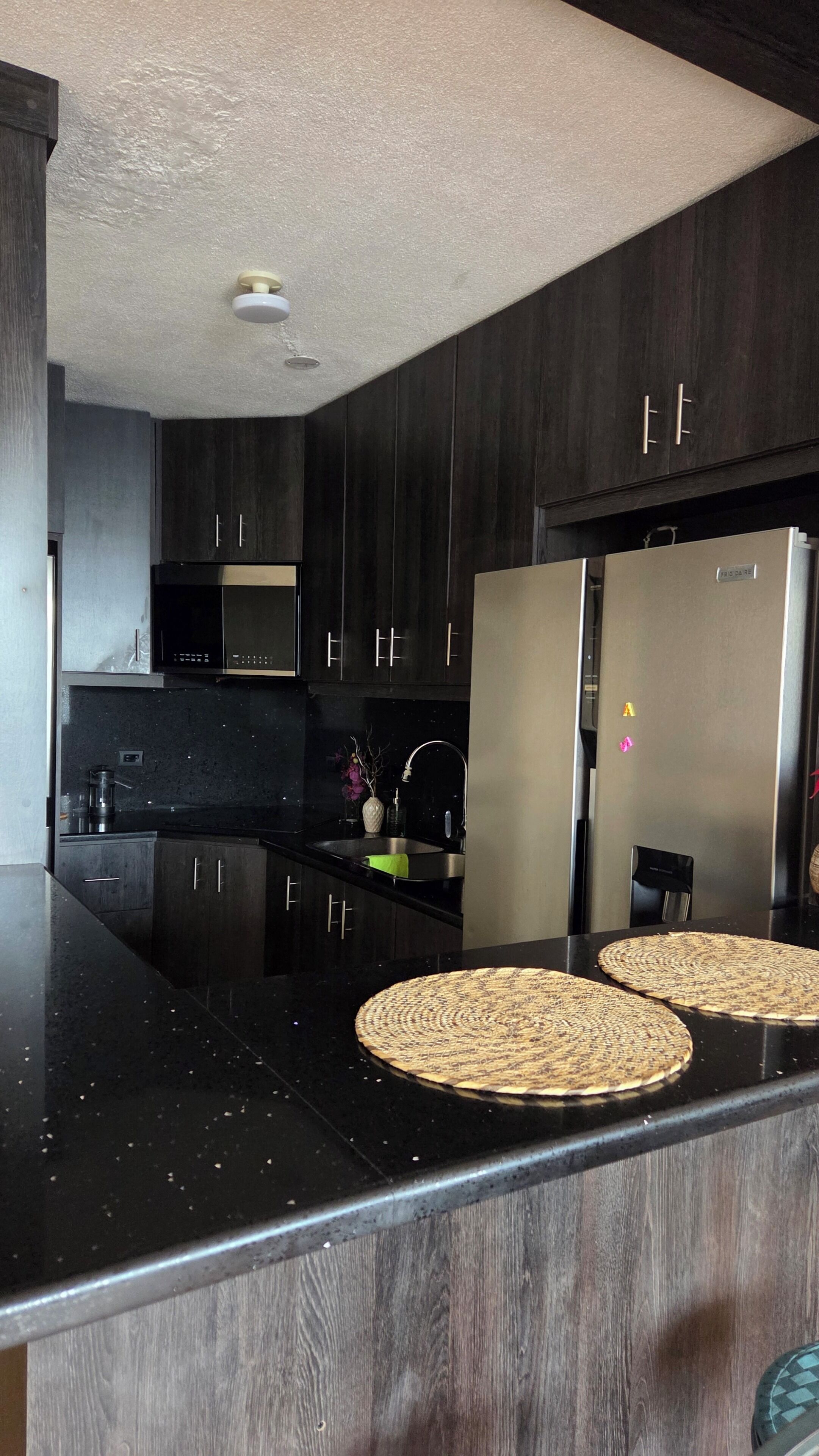 Una cucina moderna con mobili in legno scuro, elettrodomestici in acciaio inossidabile e un piano di lavoro nero.