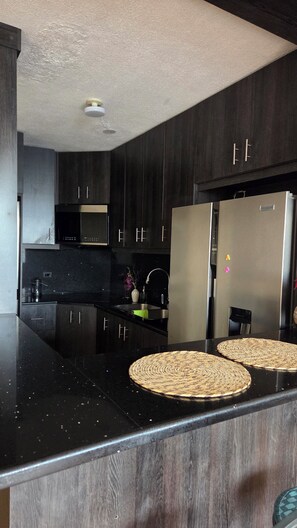 A modern kitchen with dark wood cabinets, stainless steel appliances, and a black countertop. - Drea'$ Time (Ciudad de Guatemala)