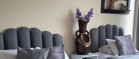 Une chambre d’hôtel avec deux lits, une literie grise, un vase décoratif avec des fleurs et une petite étagère sur laquelle est posé un cadre photo.