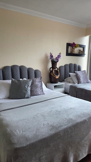 A hotel room with two beds, grey bedding, a decorative vase with flowers, and a small shelf with a picture frame. - Drea'$ Time (Ciudad de Guatemala)