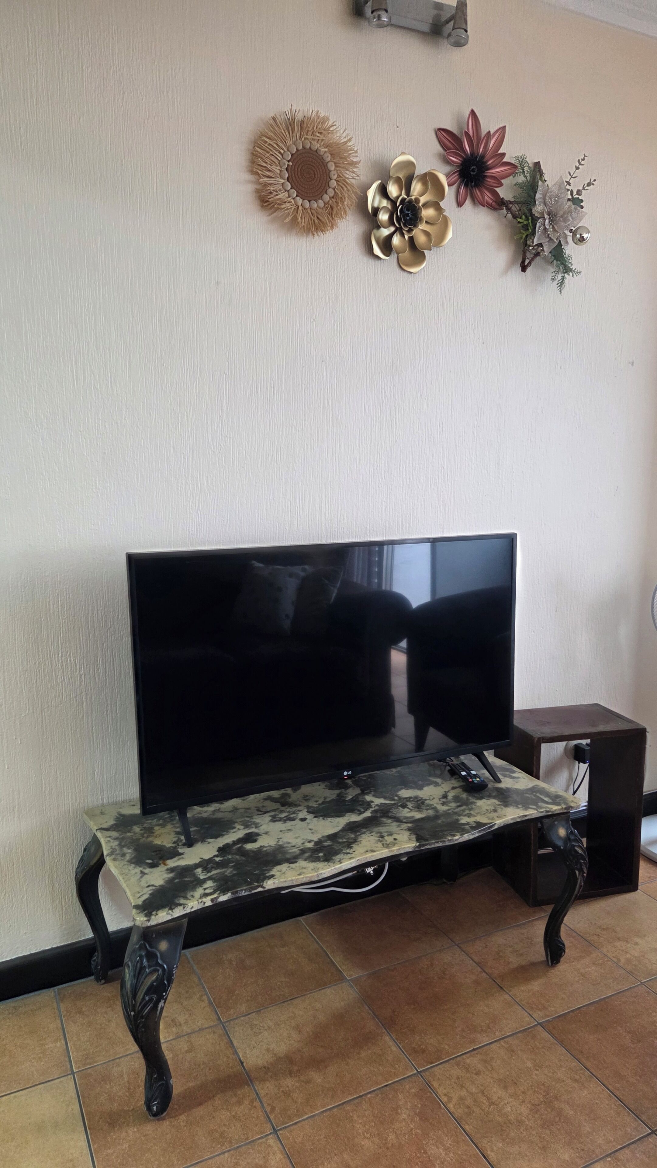 Ein Wohnzimmer mit Flachbildfernseher auf einem Tisch, einem kleinen Beistelltisch und dekorativen Wandbildern.