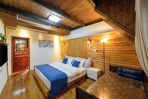 Een slaapkamer met een houten plafond, een bed met blauw beddengoed, een nachtkastje en een lamp.