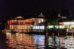 A traditional building with multiple levels, a boat docked in front, and a reflection on the water.