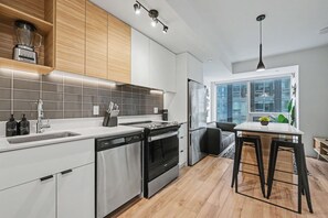 A modern kitchen with a dishwasher, stove, and refrigerator. There is a dining area with a table and chairs. - 1 Bedroom/1 Bathroom Suite (Montreal)