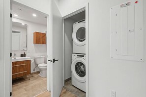 A laundry room with two stacked washing machines, a wooden cabinet, a toilet, and a mirror. - 1 Bedroom/1 Bathroom Suite (Montreal)