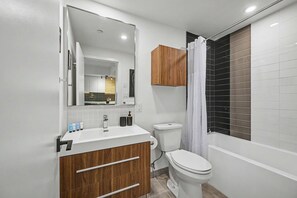 A modern bathroom with a white sink, wooden vanity, a toilet, and a shower area with a curtain. - 1 Bedroom/1 Bathroom Suite (Montreal)