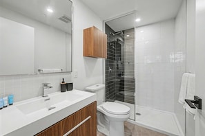 A modern bathroom with a white sink, wooden vanity, a toilet, and a glass-enclosed shower area. - 2 Bedroom/2 Bathroom Suite (Montreal)