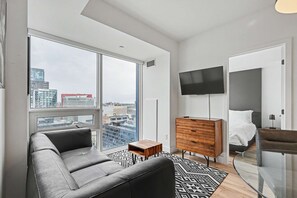 Ein modernes Wohnzimmer mit einer Couch, einem Fernseher, einer Holzkommode und einem Bett mit Kopfteil.