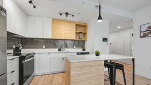 Ett modernt kök med vita skåp, en vägg med träpanel som accent, en inbyggd köksö och en barstol.