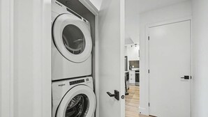 Ett tvättrum med två Whirlpool-tvättmaskiner och torktumlare placerade ovanpå varandra, en vit dörr och en hall som leder till ett köksområde.