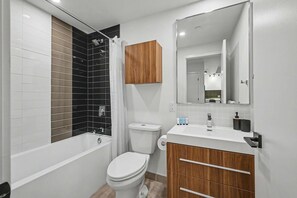 A modern bathroom with a bathtub, toilet, vanity, and a large mirror. - 2 Bedroom/2 Bathroom Suite (Montreal)