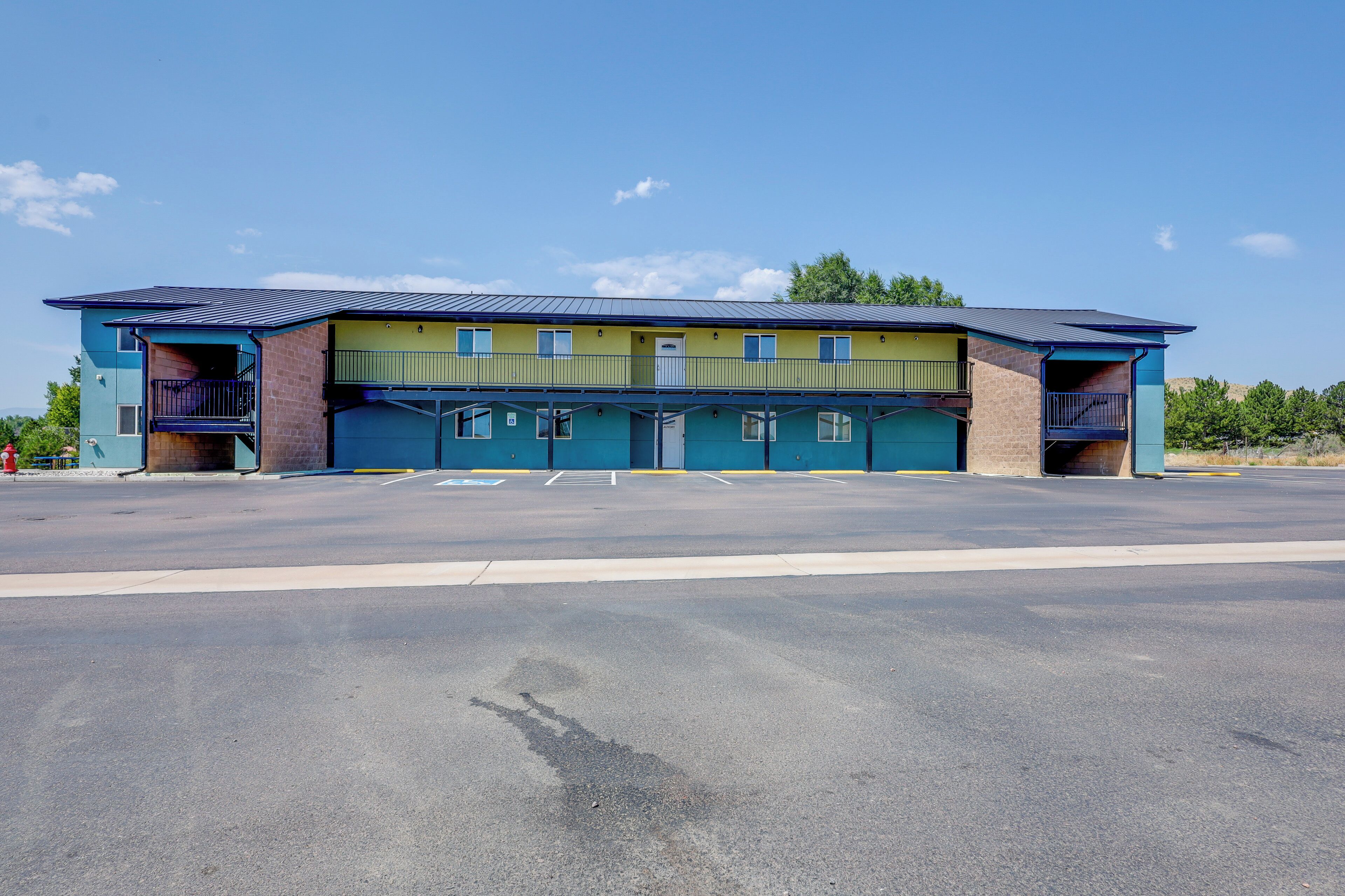 A two-story building with a flat roof, a parking lot in front, and a clear sky.