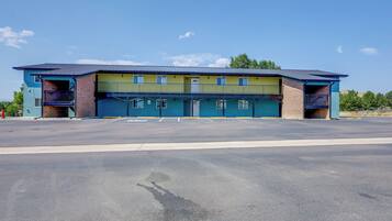 A two-story building with a flat roof, a parking lot in front, and a clear sky.