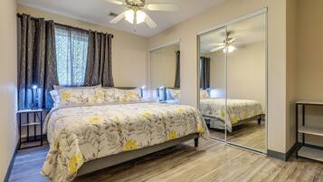 A bedroom with a bed, a ceiling fan, a mirror, and a window with curtains.