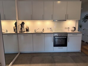 Eine moderne Küche mit weißen Schränken, einem Edelstahlbackofen und einer Kaffeemaschine.