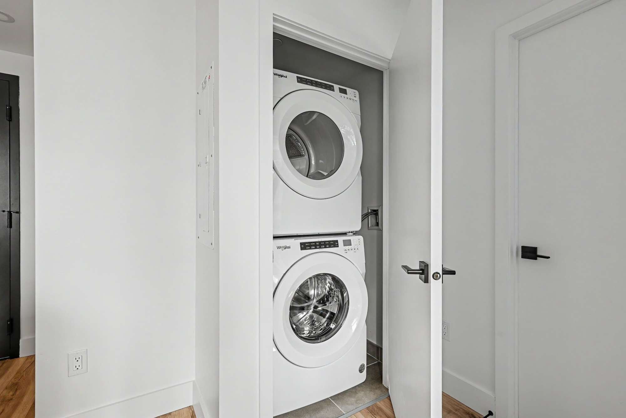 Une buanderie équipée de deux machines à laver à chargement frontal, de couleur blanche, et d’une porte donnant sur une autre pièce.