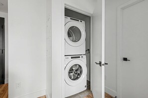 Une buanderie équipée de deux machines à laver à chargement frontal, de couleur blanche, et d’une porte donnant sur une autre pièce.