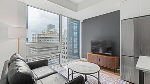 Ett modernt vardagsrum med en soffa, ett soffbord, en tv och ett stort fönster med utsikt över staden.
