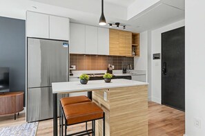 A compact kitchen with a stainless steel refrigerator, wooden cabinets, a white countertop, and a black door. - 1 Bedroom/1 Bathroom Suite (Montreal)