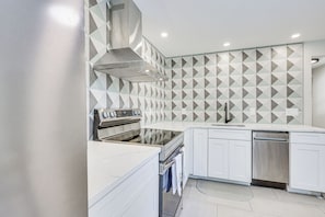 A modern kitchen with a built-in oven, stainless steel appliances, and a geometric backsplash.