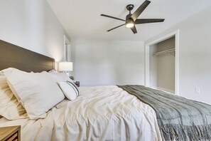 A hotel room with a bed, a ceiling fan, a nightstand, a lamp, and a closet.
